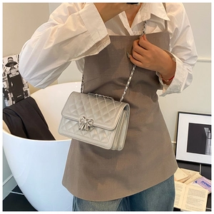 Close-up of a silver quilted crossbody bag with a metal bow clasp and chain strap