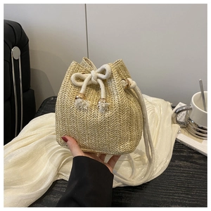 Detail of woven straw bucket bag with white drawstring closure and tassel accent