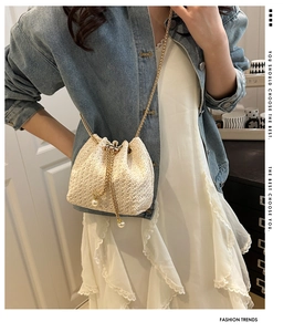 Detail of straw bucket bag with golden chain strap and elegant pearl drawstring accents