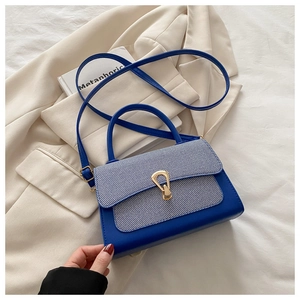 Detail of color-block handbag with striped flap and gold buckle on a cream blazer