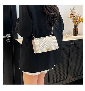 Detail of cream quilted crossbody bag with golden clasp and chain strap on shoulder