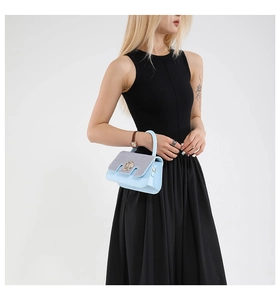 Detail of light blue crossbody bag with glitter flap and golden logo buckle worn by model