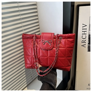Detail of red quilted shoulder bag with metal chain strap and silver bow decoration