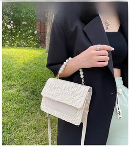 Outdoor close-up of a beige straw texture handbag with elegant pearl beaded handle