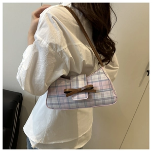 Detail of pink plaid underarm bag featuring a brown leather bow and fabric texture