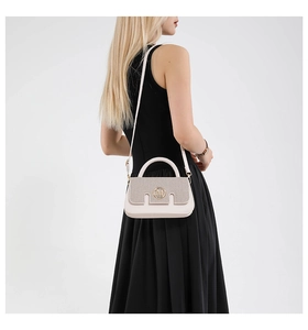 Detail of beige flap bag featuring a golden M logo and textured surface on a model