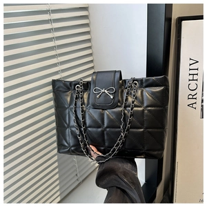 Detail of black quilted tote bag featuring a silver metal bow and luxury chain strap