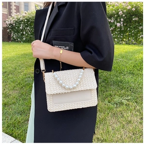 Detail of beige woven crossbody bag featuring a large pearl handle and leather strap