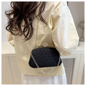 Detail of black textured crossbody bag featuring crystal buckle and gold chain strap