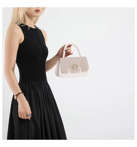 Detail view of cream white handbag with golden M logo and sparkling sequin texture flap