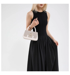 Close-up of cream handbag with textured flap and golden M-letter metal hardware