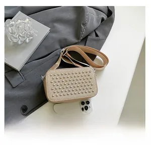 Detail view of a beige studded crossbody camera bag showing compact size near a smartphone