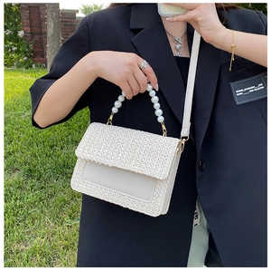 Detailed close-up of woven straw handbag with pearl handle and cream leather flap