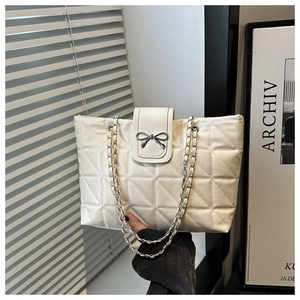Detail of white quilted tote bag featuring a silver metal bow and chain shoulder strap