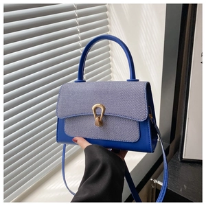 Detail of contrasting navy blue patchwork handbag with a golden horseshoe-shaped metal buckle