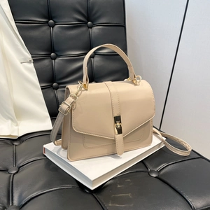 Bolso de mano beige minimalista con cierre dorado colocado sobre libros blancos