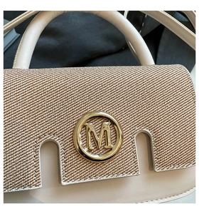 Detailed close-up of woven flap and gold M logo on stylish cream leather handbag