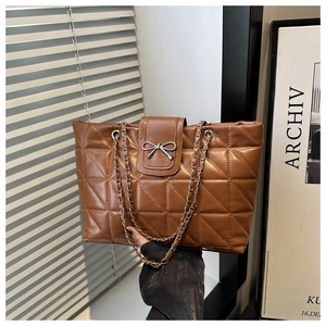 Detail of brown quilted tote bag featuring metal bow buckle and chain leather strap
