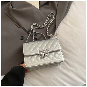 Detail of silver quilted crossbody bag featuring a metallic bow clasp and chain strap