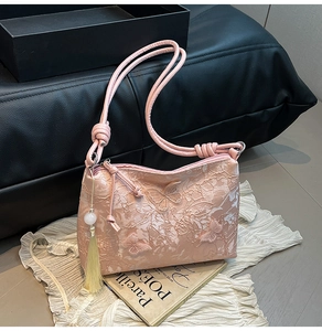 Detail of pink shoulder bag featuring butterfly lace embroidery and a beaded tassel charm