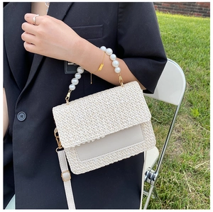 Detail of cream woven handbag with large pearl handle and leather trim in outdoor setting