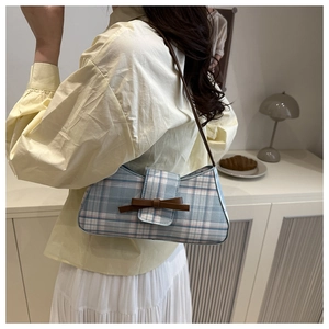 Detail of plaid underarm bag with brown leather bow and strap on a yellow shirt
