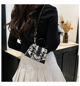 Detail of snake print crossbody bag with black flap and gold studs on a model