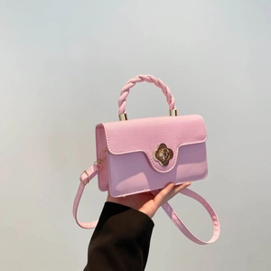 Pink leather crossbody bag with twisted handle and gold flower lock on grey background