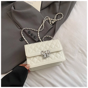 Detail of white quilted chain bag with silver bow buckle on grey blazer background