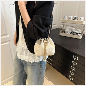 Detail of straw woven bucket bag with gold chain strap and pearl drawstring tassels