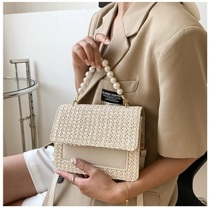 Detail of woven pearl handbag featuring white beads handle and leather logo patch
