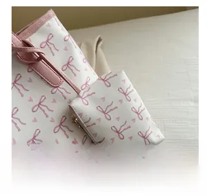 Close-up of white tote bag with pink bow print and matching mini pouch with gold zipper