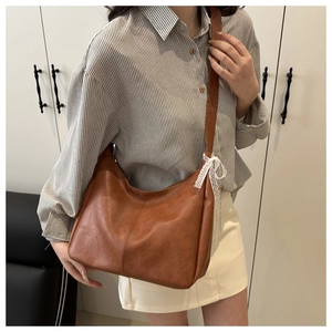Close-up of brown textured leather tote bag featuring a decorative white lace bow detail