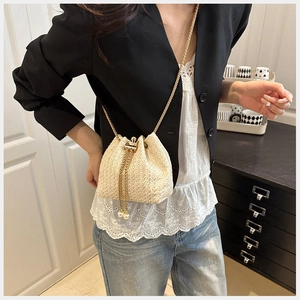 Detail of straw bucket bag featuring gold chain strap and pearl drawstring accents