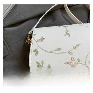 Detail of white fabric bag featuring pink floral embroidery and golden metal hook