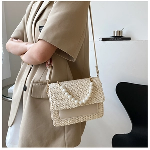 Detail of beige woven crossbody bag featuring a decorative pearl handle and leather strap