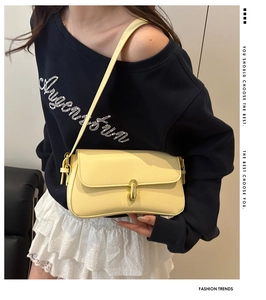 Detail of light yellow leather shoulder bag with sleek gold metal clasp and curved base