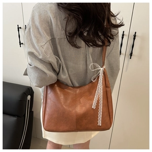 Close-up of brown textured PU leather tote bag with white lace bow detail on side
