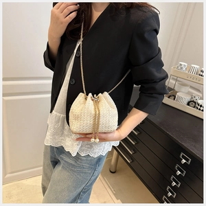 Detail of cream straw bucket bag with oversized pearl drawstring and gold chain strap