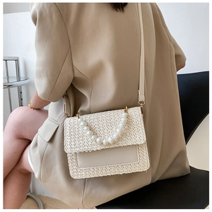 Detail of woven beige handbag with elegant pearl handle shown in a fashion lifestyle setting