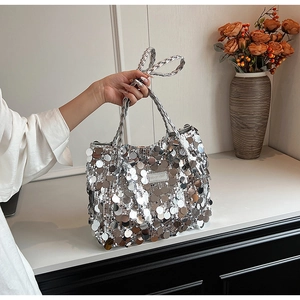 Close-up of a silver sequined tote bag featuring a metallic logo and braided handle