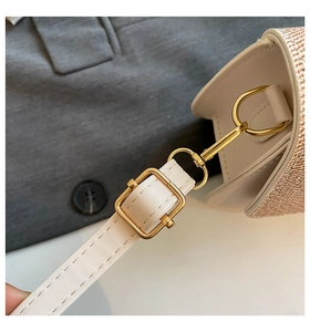 Close-up of golden hardware clasps and beige leather shoulder strap on a fashion handbag