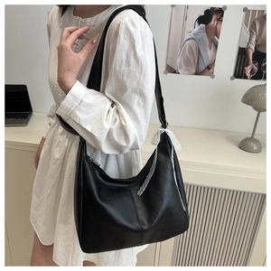 Detail of black faux leather crescent bag with white lace bow charm worn by a model