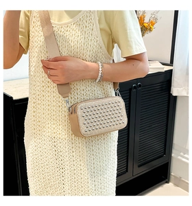 Detail of trendy beige crossbody bag with silver studs and a wide textile strap on a model