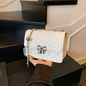 Ivory quilted crossbody bag with silver bow clasp and chain strap on black steps