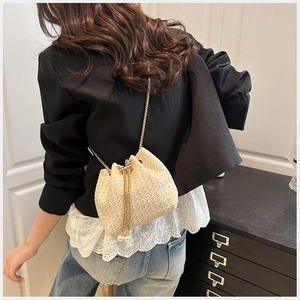 Detail of straw bucket bag with gold chain strap, drawstring and elegant pearl accents