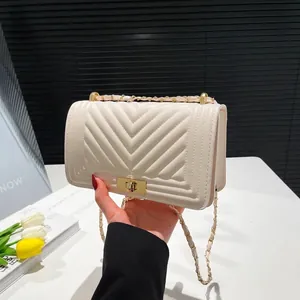 Quilted cream shoulder bag with chevron pattern and gold chain strap held in hand