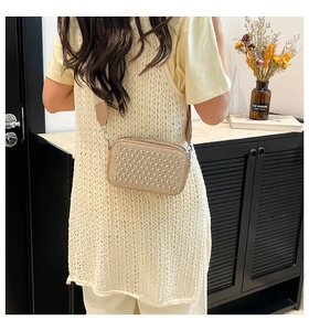 Detail of beige crossbody bag with silver studs and wide strap worn by a model