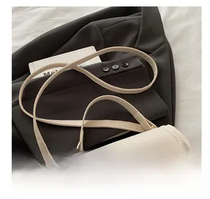 Detail of cream leather shoulder bag with thin strap and metal buckle on grey suit