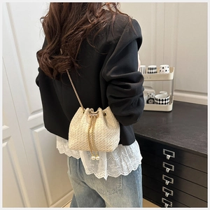 Detail of straw bucket bag featuring gold chain strap and elegant pearl drawstring charms